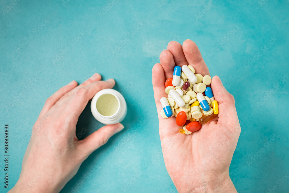 Tablets and pill bottle in woman hands, aqua background