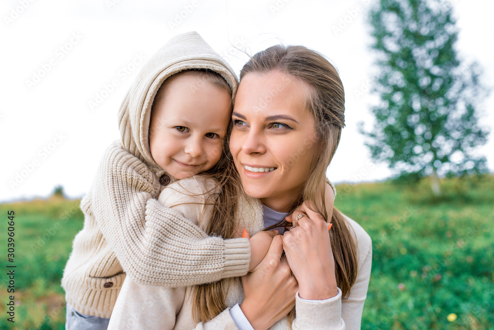 Obraz premium Little boy hugs mom happy smiling, tenderness care son, autumn day warm clothes with hood, woman mom plays with child, summer nature. Happy have fun, relax rejoice, emotions love, care, education.