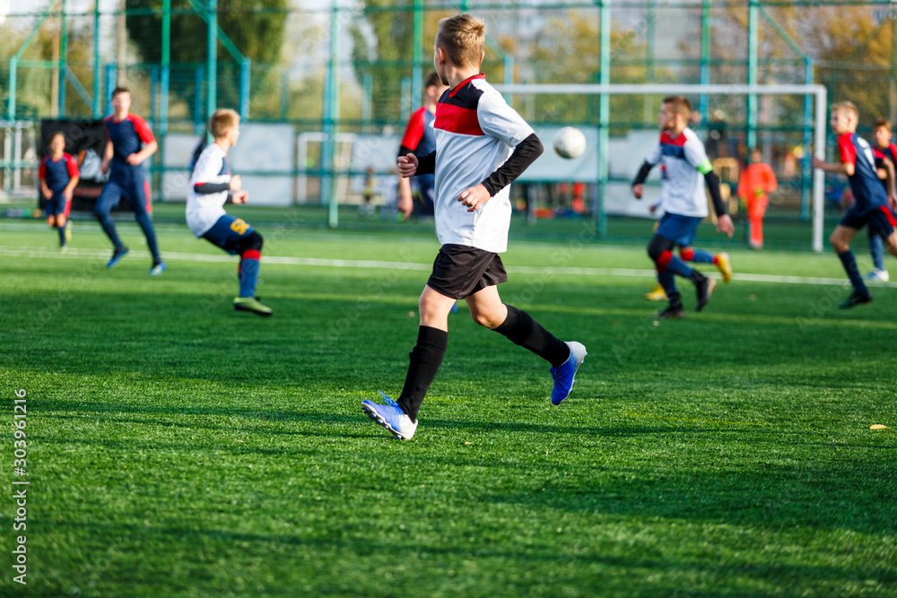 Boys in white and blue sportswear plays  football on field, dribbles ball. Young soccer players with ball on green grass. Training, football, active lifestyle for kids concept 