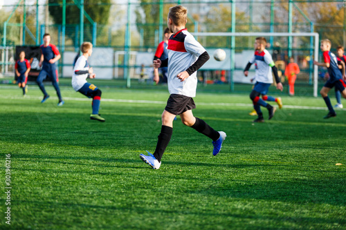 Boys in white and blue sportswear plays football on field, dribbles ball. Young soccer players with ball on green grass. Training, football, active lifestyle for kids concept 