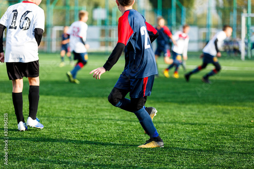 Boys in white and blue sportswear plays  football on field, dribbles ball. Young soccer players with ball on green grass. Training, football, active lifestyle for kids concept  © Natali