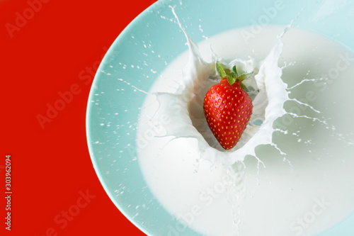 juicy sweet strawberries falling into a bowl of milk cream with splashes in all directions, copy space, red background