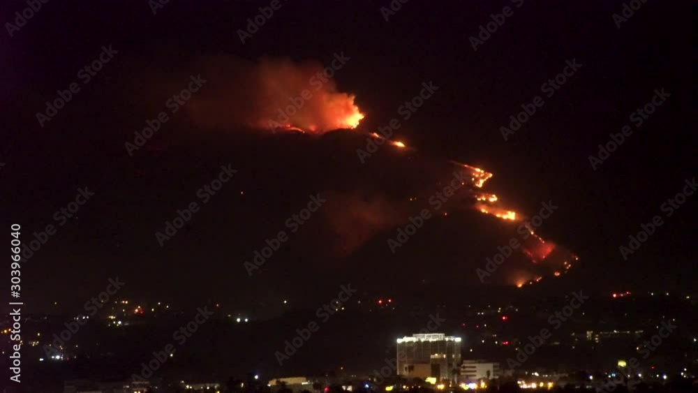 Forest fire on mountain range above residential neighborhood at night as planes dump water and smoke spreads helicopters fly around with search lights. Forest fire on mountain range above residential neighborhood at night as planes dump water and smoke spreads helicopters fly around with search lights.