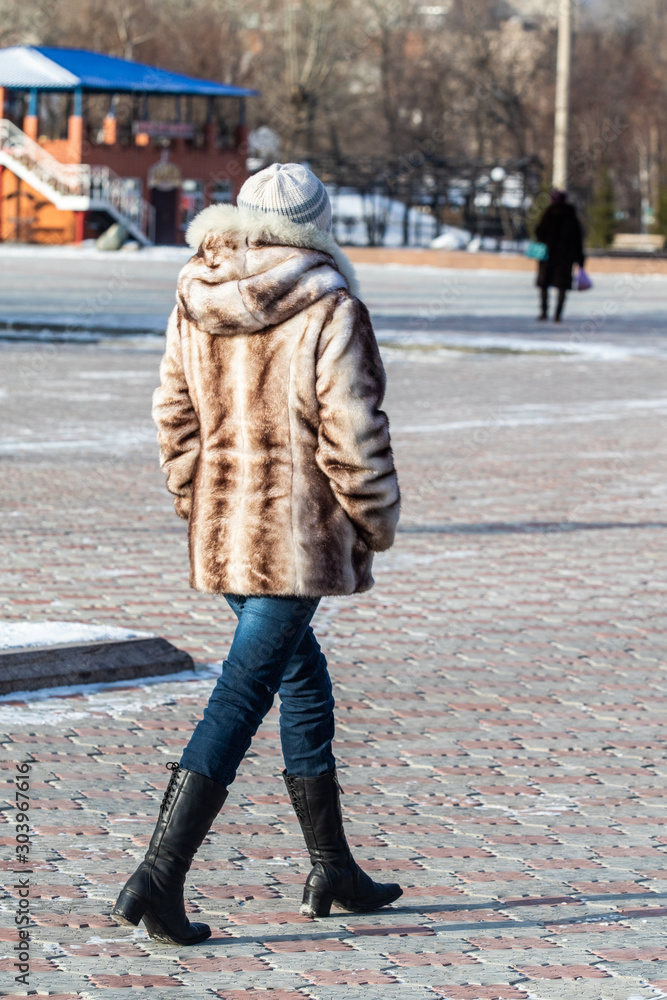 A girl in a fur coat walks along the street, autumn cold day.