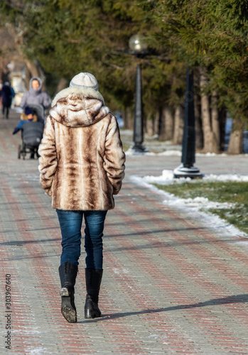A girl in a fur coat walks along the street, autumn cold day.