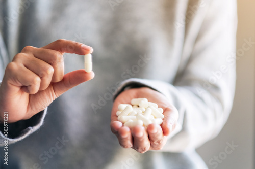 Closeup image of a woman holding and showing white medicine capsules in hand