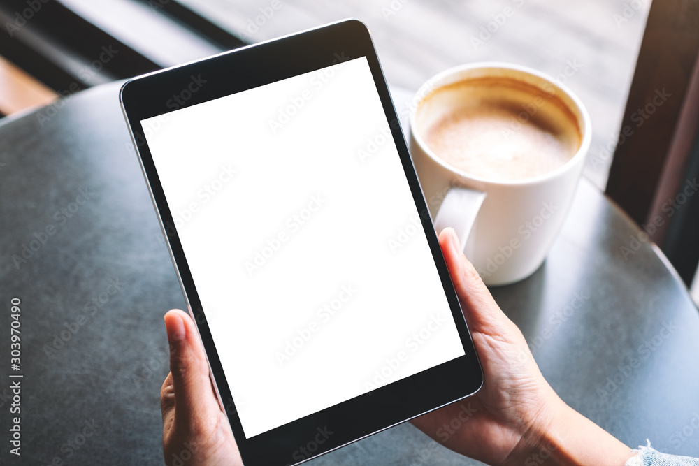 Mockup image of a woman holding black tablet with white blank screen and coffee cup on the table