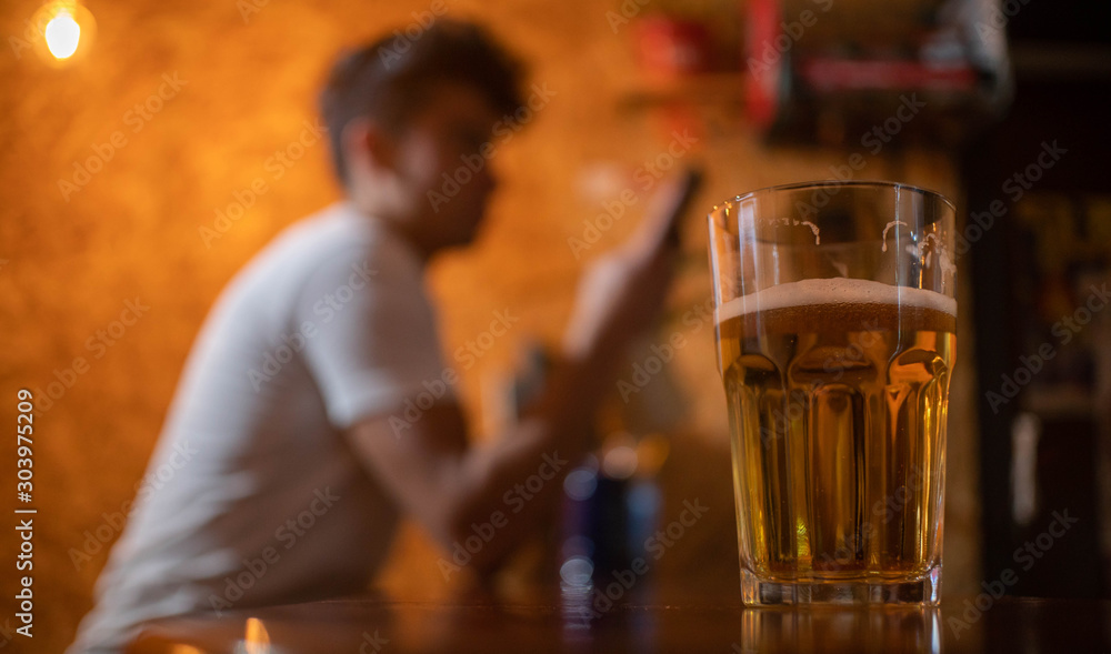 close up of a glass of beer and behind a man with a cellphone