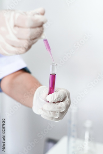 Adult hand, white glove holding glass test tube with purple liquid water, Science laboratory research study experiment project in white room background. Medical or health care pharmacy concept.