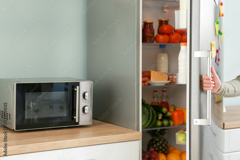 Woman opening modern fridge in kitchen Woman opening modern fridge in kitchen