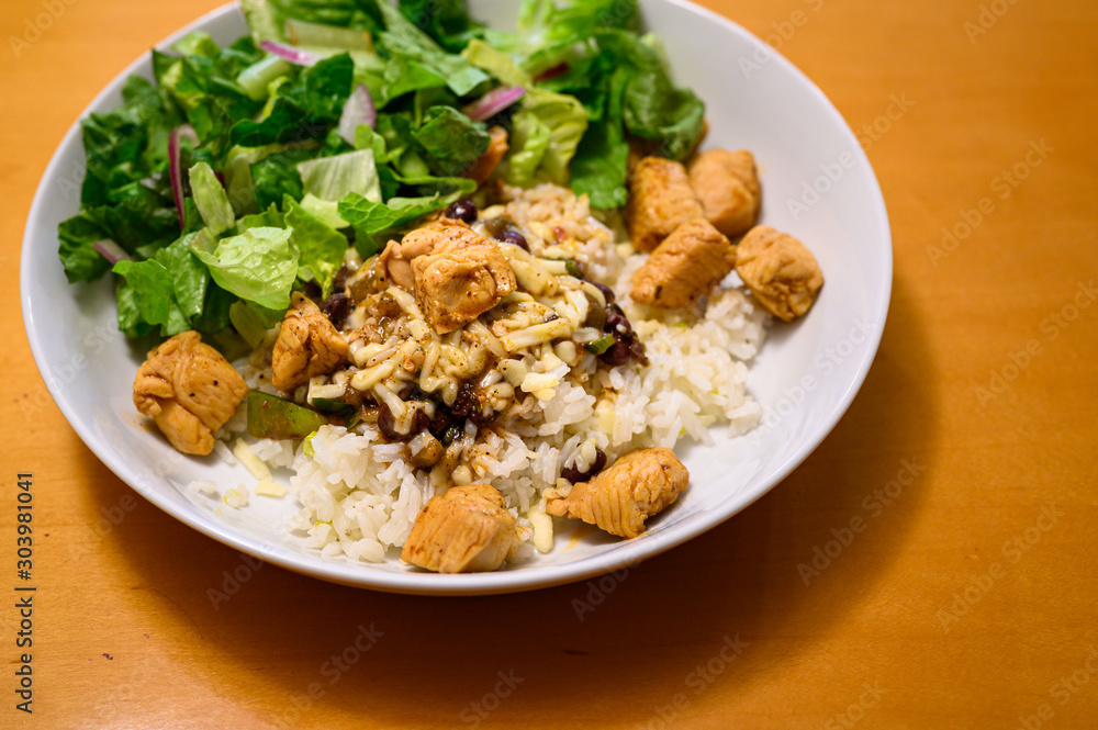 Close up of beans and rice, frijoles, with chicken, in a white bowl, with salad greens Close up of beans and rice, frijoles, with chicken, in a white bowl, with salad greens