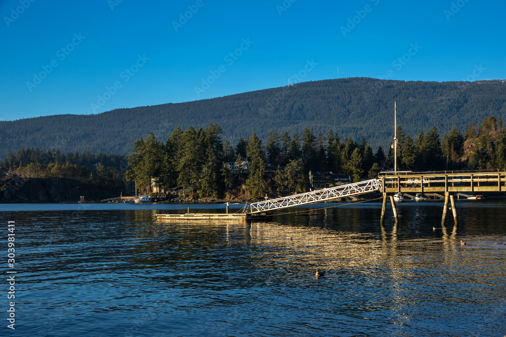 Obraz premium Pier in the bay, sunny day, sea and mountains, the harbor against the backdrop of a mountain ridge and a cloudy sky, a small village on the opposite bank