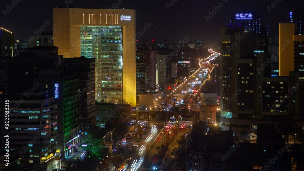 Timelapse multi-lane street road with circle of Dongcheng district surrounded by flashing Chinese advertisements on Beijing buildings at dark night