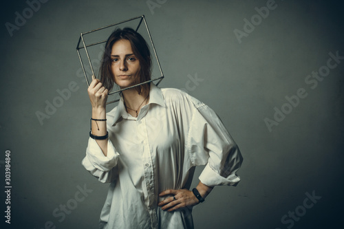 portrait of a girl in a white shirt with a metal cube-cage on his head. isolate. The concept of estrangement, the man in a case
