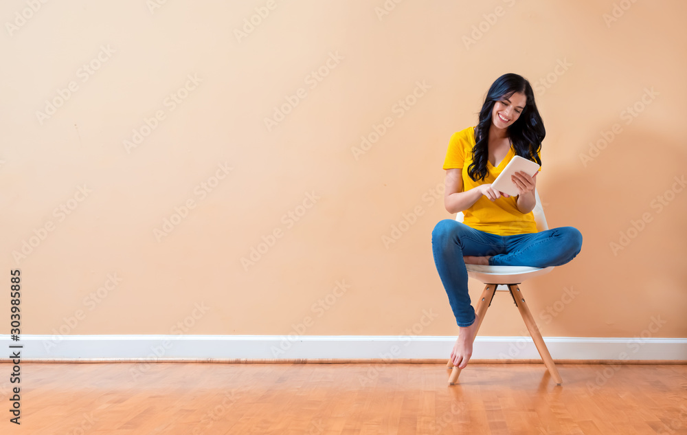 Young woman using her tablet sitting in a chair - obrazy, fototapety, plakaty 