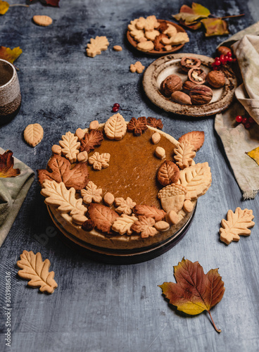 traditional pumpkin pie decorated with leaves shaped cookies on shabby blue background with coffee and textile