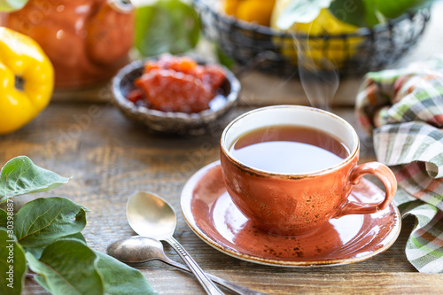 Cup of tea with homemade quince jam on an old wooden background. Fresh fruits and quince leaves on the background. Horizontal photo. rustic