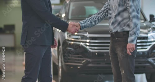 Close-up of unrecognizable male Caucasian dealer giving car keys to male customer and shaking his hand. Adult male car dealer making sale-purchase deal. Car business. Cinema 4k footage ProRes HQ. photo
