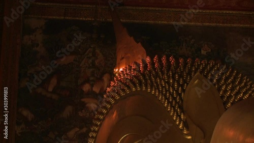 An extreme closeup shot of the face of the reclining golden Buddha in front of a mural painting on the interior walls of Wat Pho temple in Thailand. photo