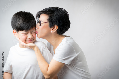 A smart looking Asian mother gently kiss her preteen son with love and tender. Mother and son bonding and love expression, Mother's day, Love mom, Raising teenager concept.