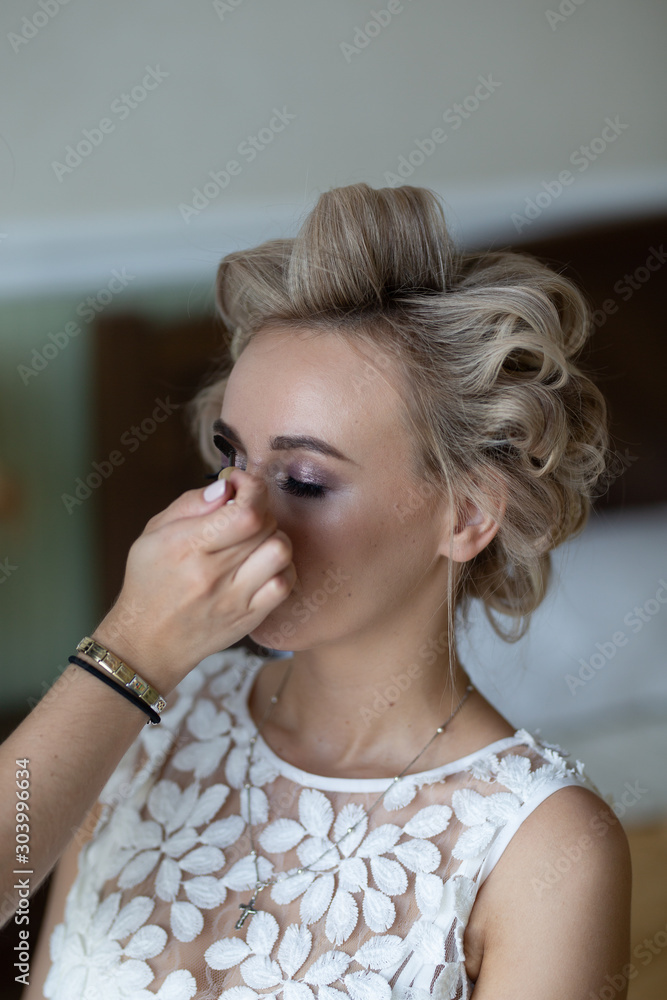 Young beautiful girl blonde bride in a sexy white boudoir dress dresses and gathers for a wedding ceremony in a hotel room while waiting for the groom. Love and lovestory.