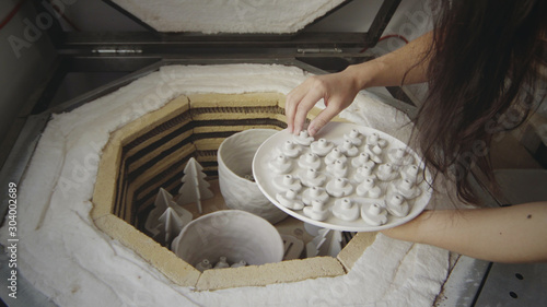 Foto Closeup of asian female master potter puts small raw clay products into a kiln for firing