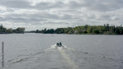 Flying above Lake of the Woods, Kenora, Ontario, Canada. Following a small boat with two people from behind in a cloudy day. 4k drone footage track in. photo