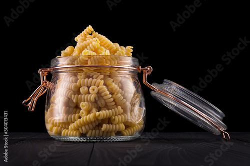 Jar of fusilli pasta on wooden table isolated on black background photo