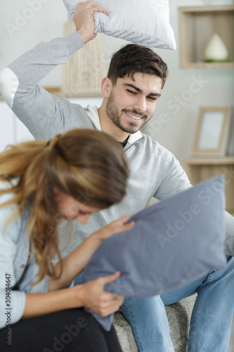 happy couple jokingly holds the pillow fight on the sofa
