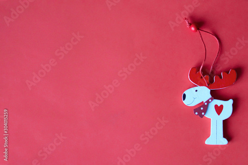 New Year and Christmas flat lay red background with wooden deer ornament and coopy space for text. White deer toy with red cord and bead. Poster and greeting card template. Red heart shape photo