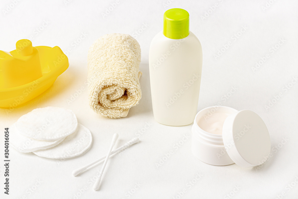 Mock up of baby bath products: bottles for shampoo (shower gel, lotion, oil), towel, cotton buds and pads on white background. Close up, copy space for text. Concept of baby bath accessories Mock up of baby bath products: bottles for shampoo (shower gel, lotion, oil), towel, cotton buds and pads on white background. Close up, copy space for text. Concept of baby bath accessories