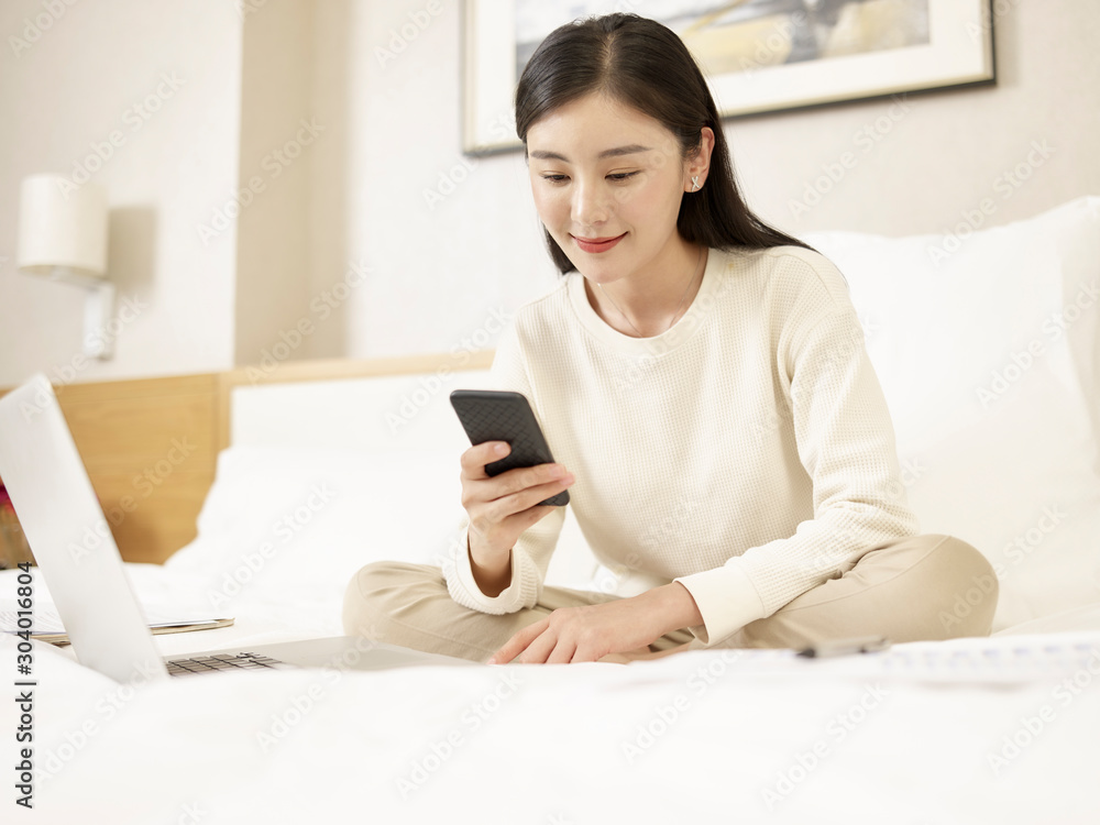 young asian woman using cellphone and laptop on bed young asian woman using cellphone and laptop on bed