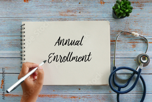 Top view of plant,stethoscope, and hand writing Annual Enrollment on notebook on wooden background. photo