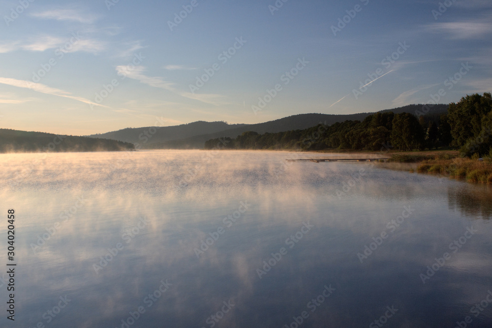Fototapeta premium Sunrise over the lake in fog, summer morning, forest in the background, Predni Vyton, Lipno lake, Czech republic