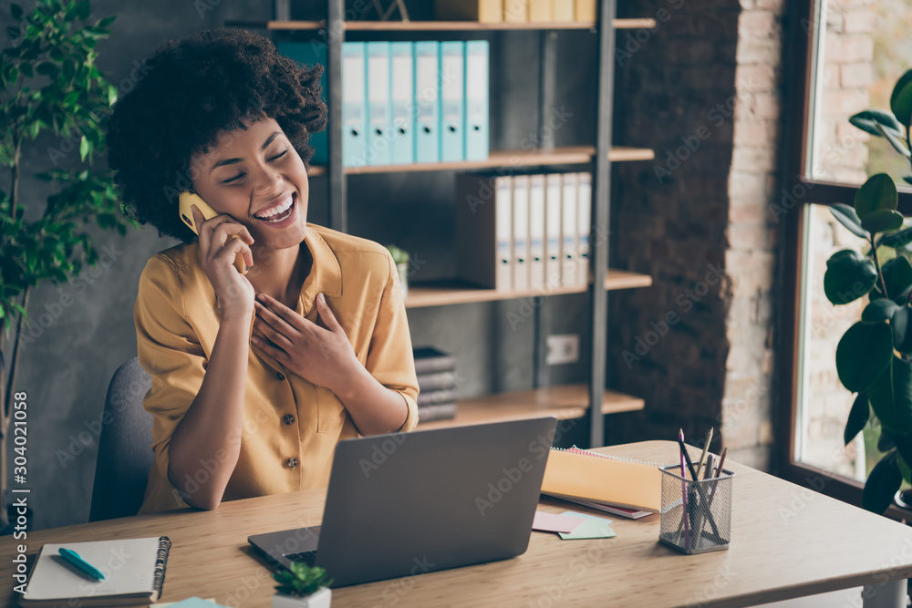 Photo of sincere cheerful mixed-race laughing girl speaking by phone with her friend colleague enjoying her break with pens notepad on desktop - obrazy, fototapety, plakaty 