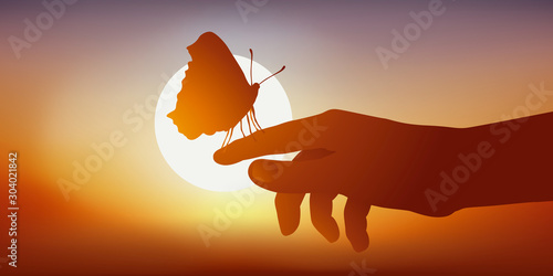 Concept de la légèreté et de la fragilité, avec la silhouette d’un papillon posé sur une main vu en contre jour face à un coucher de soleil.