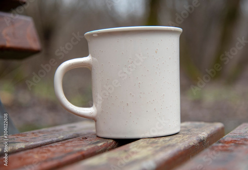 Ceramic mug on a wooden bench on a blurred background.