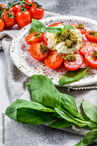 Italian cheese stracciatella (mozzarella buffalo) on small plate served with fresh tomatoes and basil. Gray background. Space for text