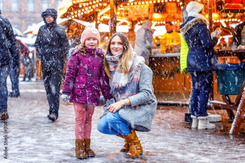 Little cute kid girl and young mother having fun on traditional German Christmas market during strong snowfall. Happy child and beautiful woman enjoying family market in Germany, Dresden