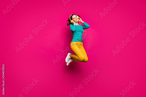 Full length body size photo of cheerful positive curly white nice cute pretty girlfriend jumping up listening to music isolated pink vibrant color background