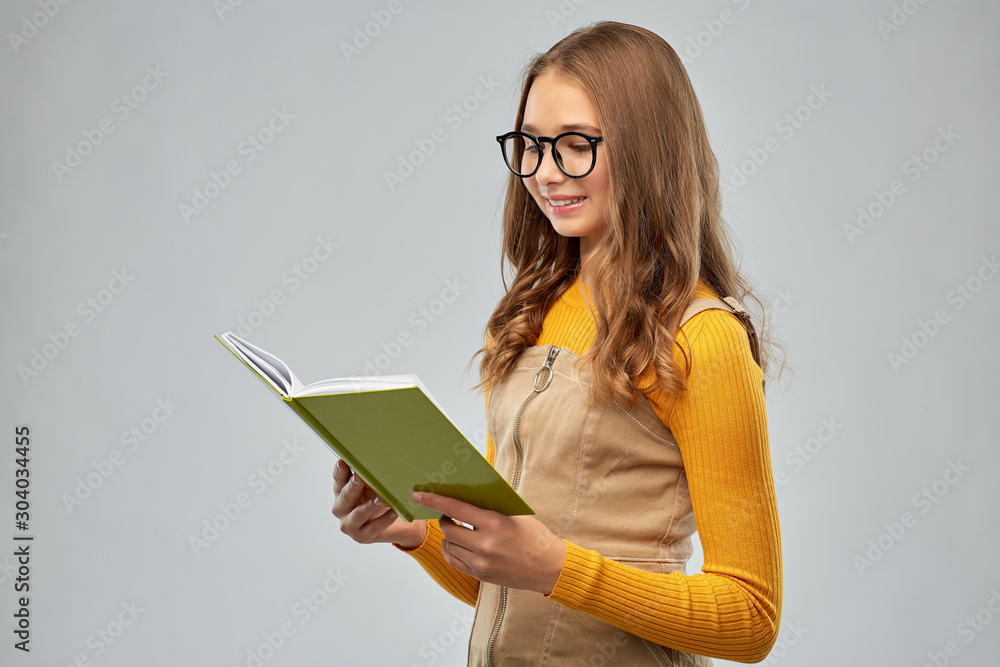 high school, education and vision concept - smiling teenage student girl in glasses reading book over grey background high school, education and vision concept - smiling teenage student girl in glasses reading book over grey background