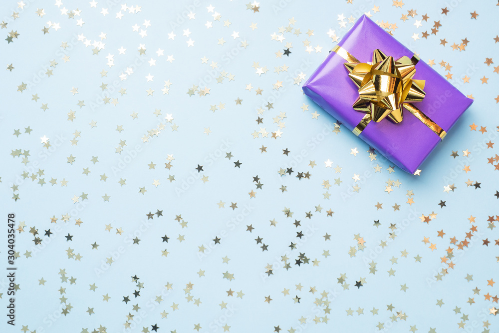 Flat lay background for celebration Christmas and New Year. Gift boxes are purple with gold ribbons bows and confetti stars on a blue background. top view copy space. Flat lay background for celebration Christmas and New Year. Gift boxes are purple with gold ribbons bows and confetti stars on a blue background. top view copy space.