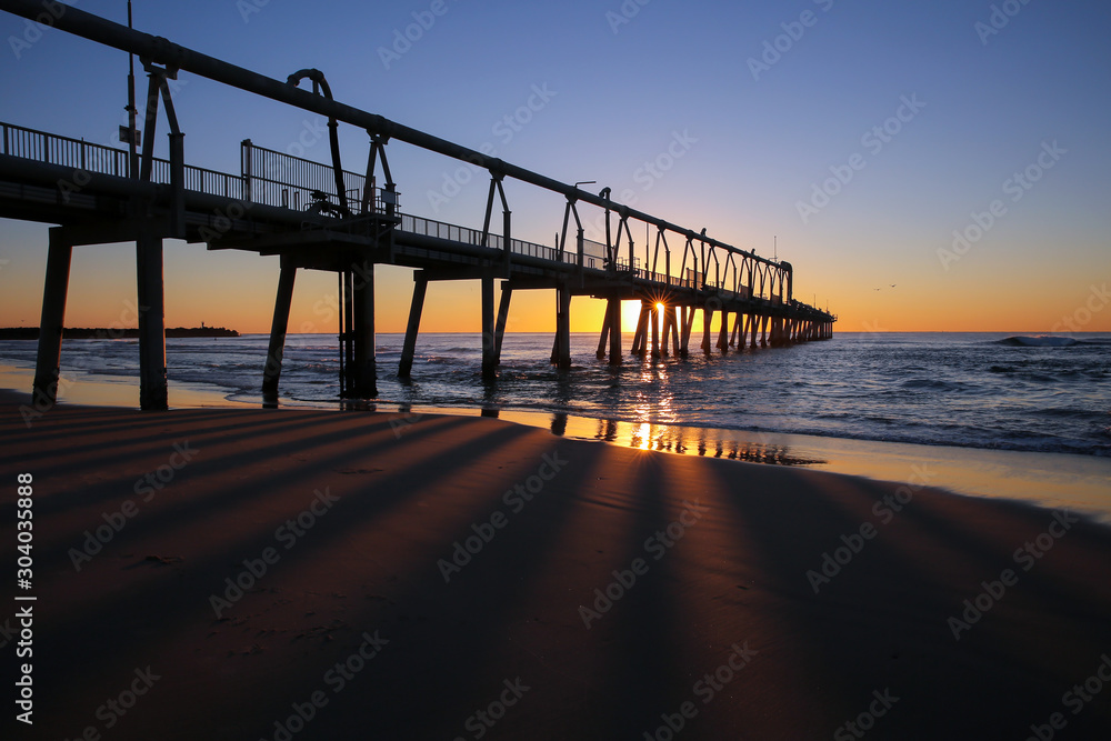 The Spit jetty on the Queensland Gold Coast at sunrise with the pylons shadows across the sand.