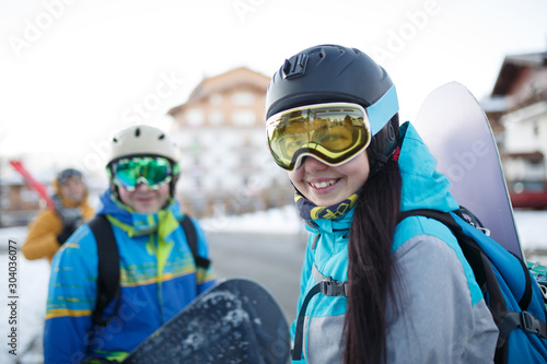 Image of happy woman in mask with snowboard in hand and men at snow resort .