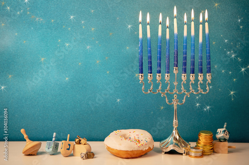 concept of of jewish religious holiday hanukkah with glittering raditional chandelier menorah, spinning top toys (dreidel), a doughnut and chocolate coins photo