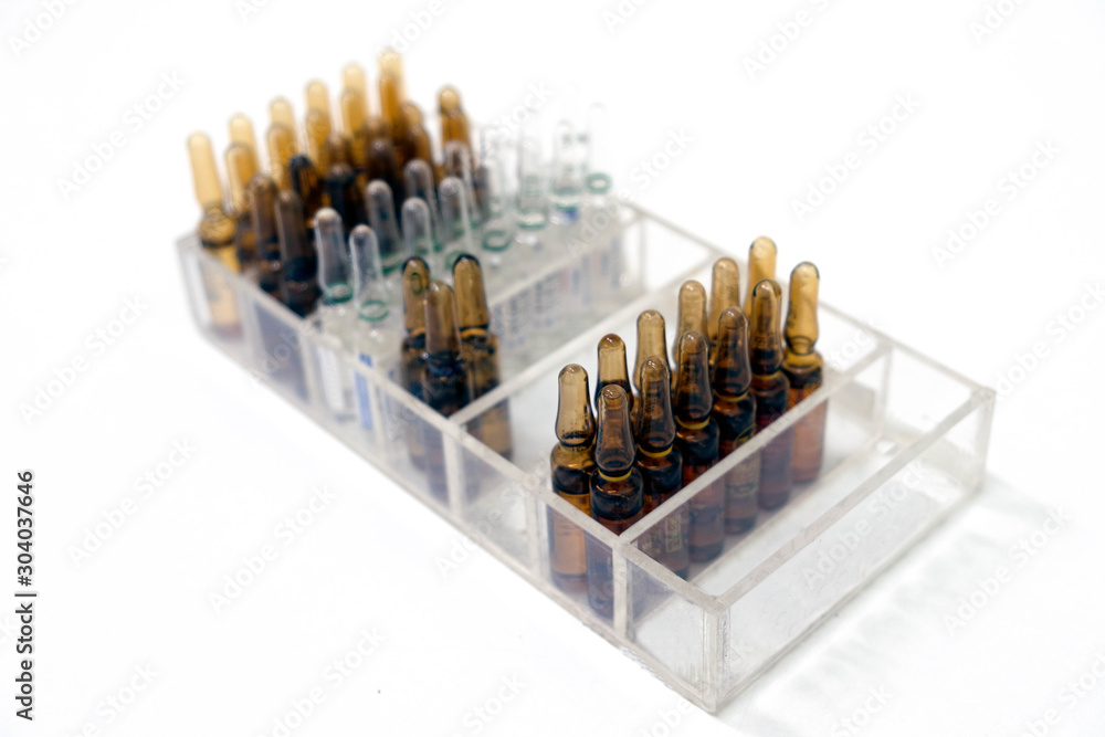 Glass bottles for medication or vaccines, waiting to be packed in a syringe for doctor in hospital to use treatment. There are brown and clear glasses arranged in a tray. Selection focus in foreground Glass bottles for medication or vaccines, waiting to be packed in a syringe for doctor in hospital to use treatment. There are brown and clear glasses arranged in a tray. Selection focus in foreground