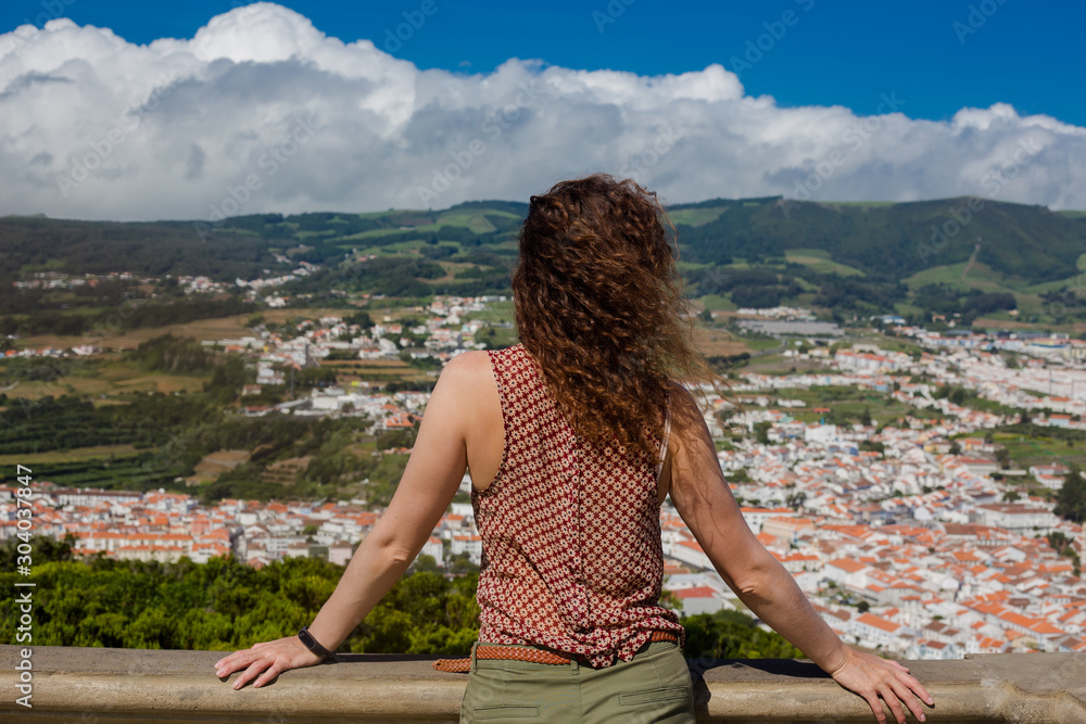 A young woman is standing in front of Angra do Heroismo, Terceira, Azores, Portugal.