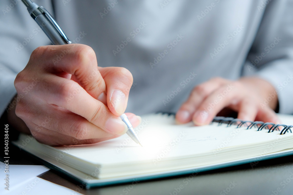 The hand of a young woman writing note of the warning message, details, things to do or preparation information of report with a bronze pen onto the book used eye preservation paper, green cover page The hand of a young woman writing note of the warning message, details, things to do or preparation information of report with a bronze pen onto the book used eye preservation paper, green cover page