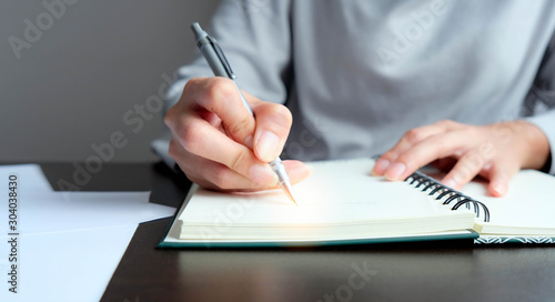 The hand of a young woman writing note of the warning message, details, things to do or preparation information of report with a bronze pen onto the book used eye preservation paper, green cover page