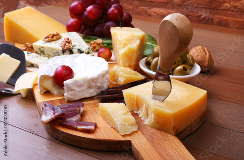 Assortment of cheese with fruits, grapes, nuts and cheese knife on a wooden serving tray. photo